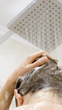 A young girl washes her hair with shampoo. A woman takes a shower. Vertical video