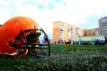 A large orange american football helmet stands close up on the green grass of the stadium - Powered by Adobe