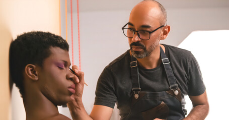 Male makeup artist doing makeup on an African transgender person.