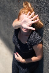 A woman in a gray dress on a gray background. The woman has an outstretched hand covering her face.