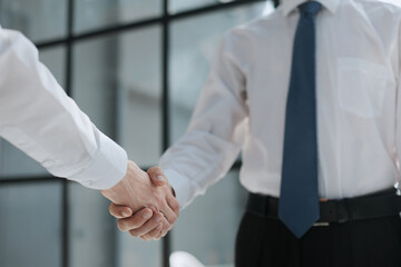 Fototapeta premium Two businessmen shake hands on the background of empty modern office, signing of a contract concept, close up