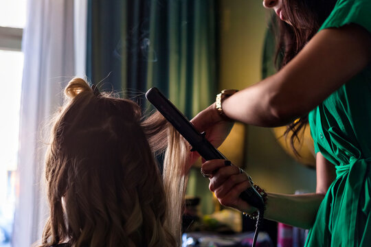 Close-up of hairdresser female create make fashionable hairdress for pretty middle age lady at home. Barber woman making hairstyle in dark living room. Concept of hairstyle, lifestyle. Copy text space