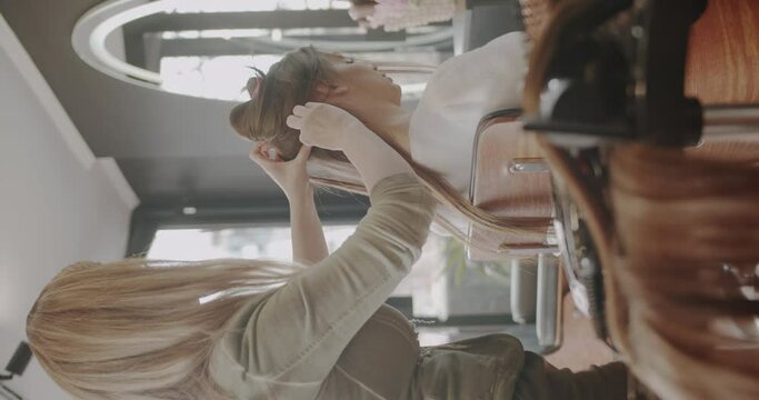 Adding hair extensions to a brunette lady, professional hair styling salon, vertical video, trucking motion