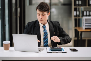 Businessman working with laptop and using a calculator to calculate the numbers of static in office. Finance accounting concept.