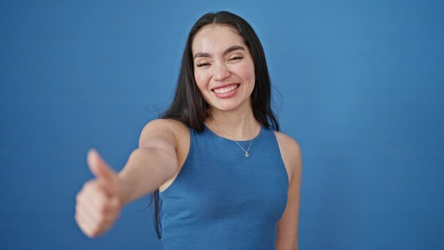 Young beautiful hispanic woman smiling confident doing ok sign with thumb up over isolated blue background