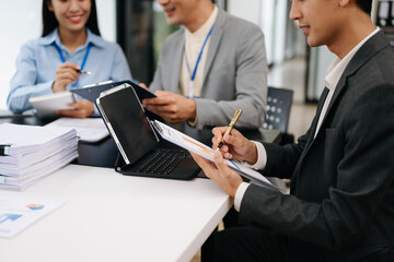Fototapeta premium Business documents on office table with smart phone and laptop and two colleagues discussing data in the background in morning light