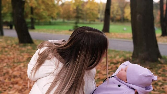 Young mother with newborn baby in autumn park. Mother shakes the child in her arms so that the girl does not cry. Slow motion horizontal video