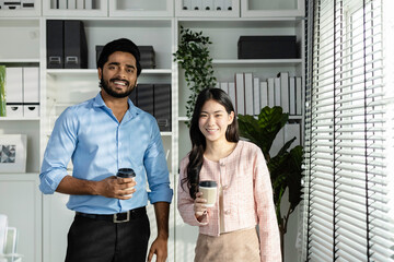 Man indian and asian woman holding coffee cup talking for work relax time standing in modern office. Asian business people meeting talking brainstorming together in office Teamwork concept.