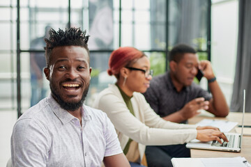 Fototapeta premium young African American man posing for the camera while sitting at a table in front of his colleagues