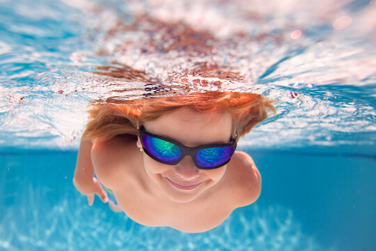 Child in swimming in pool. Funny little boy swims underwater in the pool. Underwater kids portrait from under the water. Summer holiday. Kids weekend.