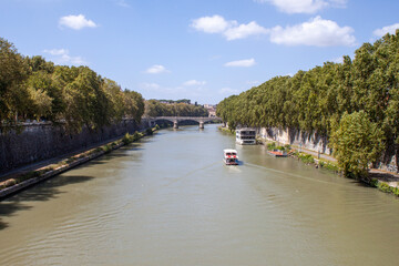 Fototapeta premium Rome, Italy - August 06, 2023: View of the Tiber from Ponte Sisto on a sunny day, cloudy water and a boat going up the river.