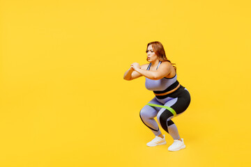 Fototapeta na wymiar Full body sideways young chubby plus size big fat fit woman wear blue top warm up training use elatic band for legs do squats isolated on plain yellow background studio home gym Workout sport concept.