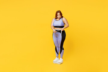 Fototapeta na wymiar Full body sad young plus size big fat fit woman wear blue top warm up train stand on scales check result look at measure tape isolated on plain yellow background studio home gym Workout sport concept.