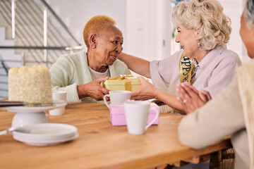 Senior friends, birthday cake and women celebration at a home with a present and gift with people. Surprise, giving and party of elderly group at a dining room table together in retirement with smile