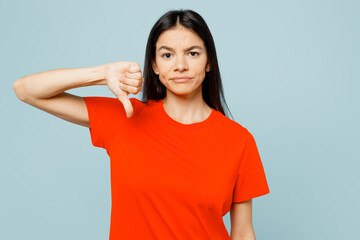 Young dissatisfied displeased latin woman wear orange red t-shirt casual clothes showing thumb down dislike gesture isolated on plain pastel light blue background studio portrait. Lifestyle concept.