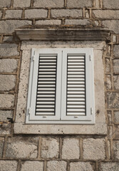 Fototapeta na wymiar Traditional new white window shutters as blinds on old stone home