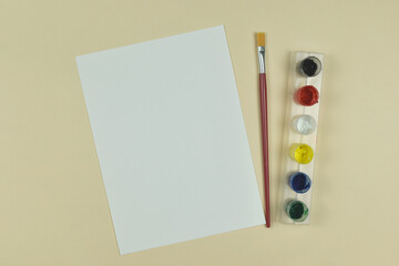 Top view of art palette, watercolor and a brush on orange background and copy space.
