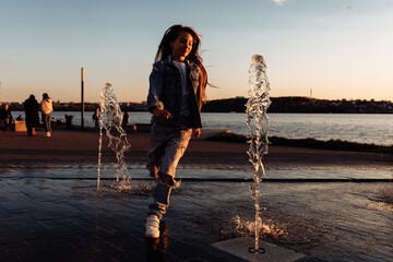 A little beautiful girl runs happily in torn jeans with long flowing hair against the background of a golden sunset.