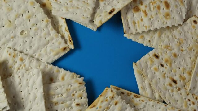 Matzah or Matzo kosher food on blue background with David Star. Jewish traditional Passover bread. Pesach celebration symbol. 4K Video, Rotating.