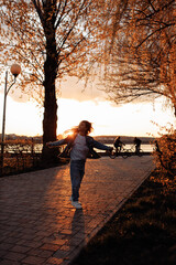 A little beautiful girl runs happily in torn jeans with long flowing hair against the background of a golden sunset.
