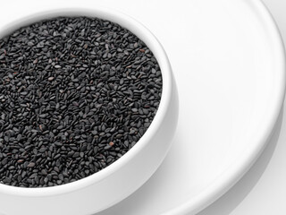 Black sesame seeds in a white bowl on a white tray on a white background. Horizontal. Selective focus. Close-up. Incline.