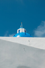 Close up of the dome of a Greek Orthodox Church in Santorini.  Half sky with dome, blue colour and half whitewashed wall.  