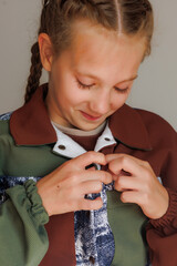 A little girl with blond long hair in two pigtails buttons up a demi-season jacket for a product demonstration