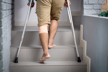 Closeup leg young asian man walking on stair with crutch at home, close-up man walking while...
