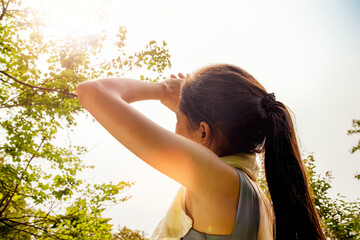 Back view Asian woman doing sport jogging feeling sun and heat too hot during jogging in park sweltering summer weather covering face with hands covering face against UV rays.