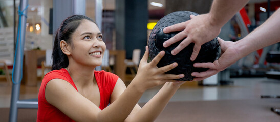 Young asian woman and caucasian man or trainer doing abs with ball with determination together in fitness gym, workout and exercise for strength and strong of muscular, weight training sport concept.