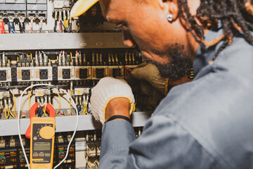 African male electrician engineer working inspect electrical system control cabinet industria...