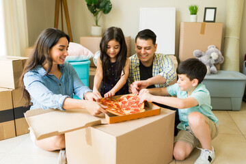 Cheerful family taking a break and eating pizza together after unpacking boxes while moving into a new house or apartment