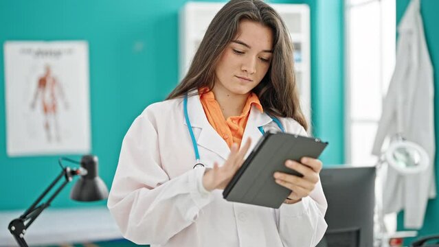 Young beautiful hispanic woman doctor using touchpad at clinic