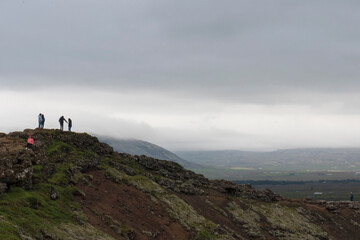 People walking on upper ridge of the volcanic Kerid Crater overlooking the crater lake in the Grimsnes area of South Iceland. 