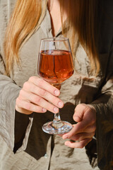 Glass of rose wine in the hands of a girl in the rays of the setting sun at home. Tasting of alcoholic beverages. Celebrate and enjoy the moment. Romantic evening aperitif. Close-up glass of wine