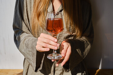 Glass of rose wine in the hands of a girl in the rays of the setting sun at home. Tasting of alcoholic beverages. Celebrate and enjoy the moment. Romantic evening aperitif. Close-up glass of wine
