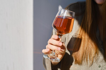 Glass of rose wine in the hands of a girl in the rays of the setting sun at home. Tasting of alcoholic beverages. Celebrate and enjoy the moment. Romantic evening aperitif. Close-up glass of wine
