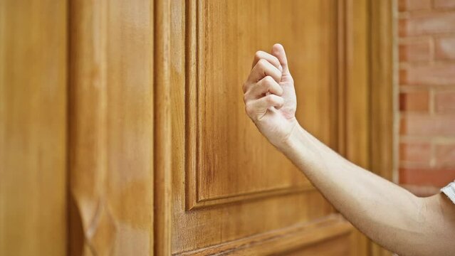 Young hispanic man knocking the door at street