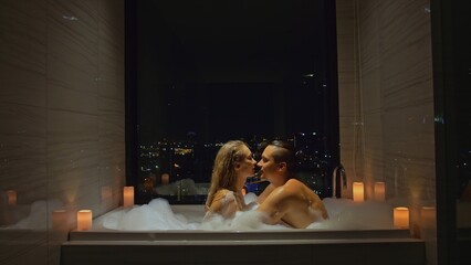 Young love couple enjoys romantic honeymoon in hotel. Married couple relax in bathtub with view of...