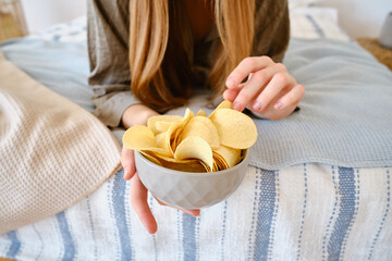 A girl eats crispy potato chips from a bowl on the couch. Quick snack. Calories and diet