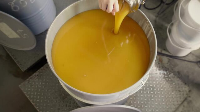 Factory worker feeling a barrel with homogenized honey with many barrels on the background