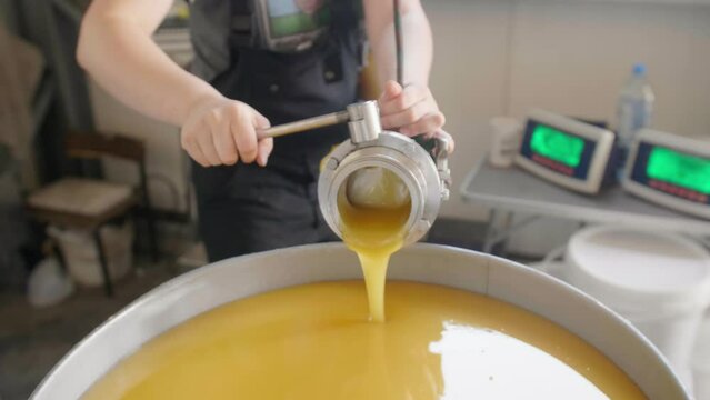 Factory worker feeling a barrel with homogenized honey with many barrels on the background