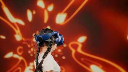 The girl wearing VR headset in virtual reality. The cute little child in modern virtual reality paint and fly. Blur background. Concept paint, fly in VR headset, children leisure in virtual reality