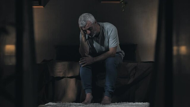 anxiety depression troubled male sits on bed in the dark at night,mature man can't sleep because of his concern thoughts