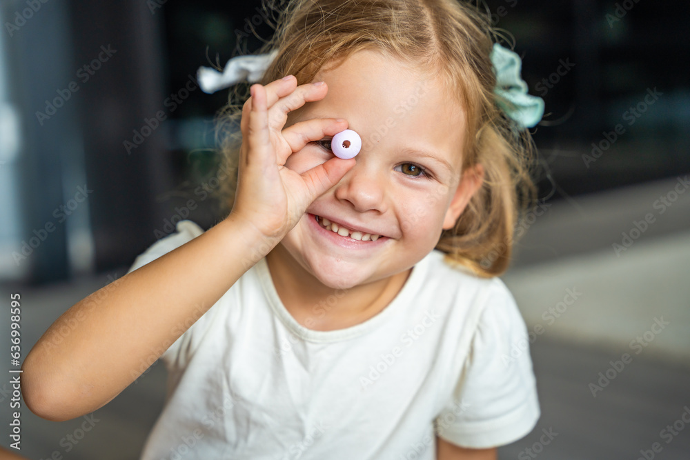 Wall mural Little girl plays with bead making wooden beads bracelet. Children's creativity and the development of fine motor skills