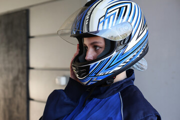 Girl racer stands in a helmet in a racing garage with a raised visor