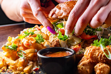 woman chef hands cooking fast food set on plate. burger, potato chips, french fries, chicken wings, fried cheese and more on table.