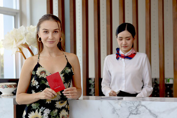 Happy beautiful tourist woman customer showing passport during checking in at hotel reception...