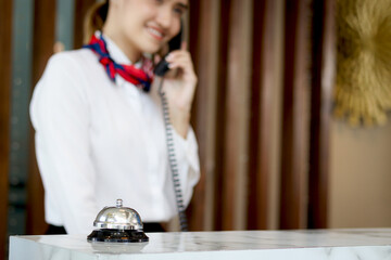 Silver bell on hotel reception service desk with blurred background of smiling Asian female...