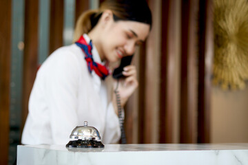 Silver bell on hotel reception service desk with blurred background of smiling Asian female...